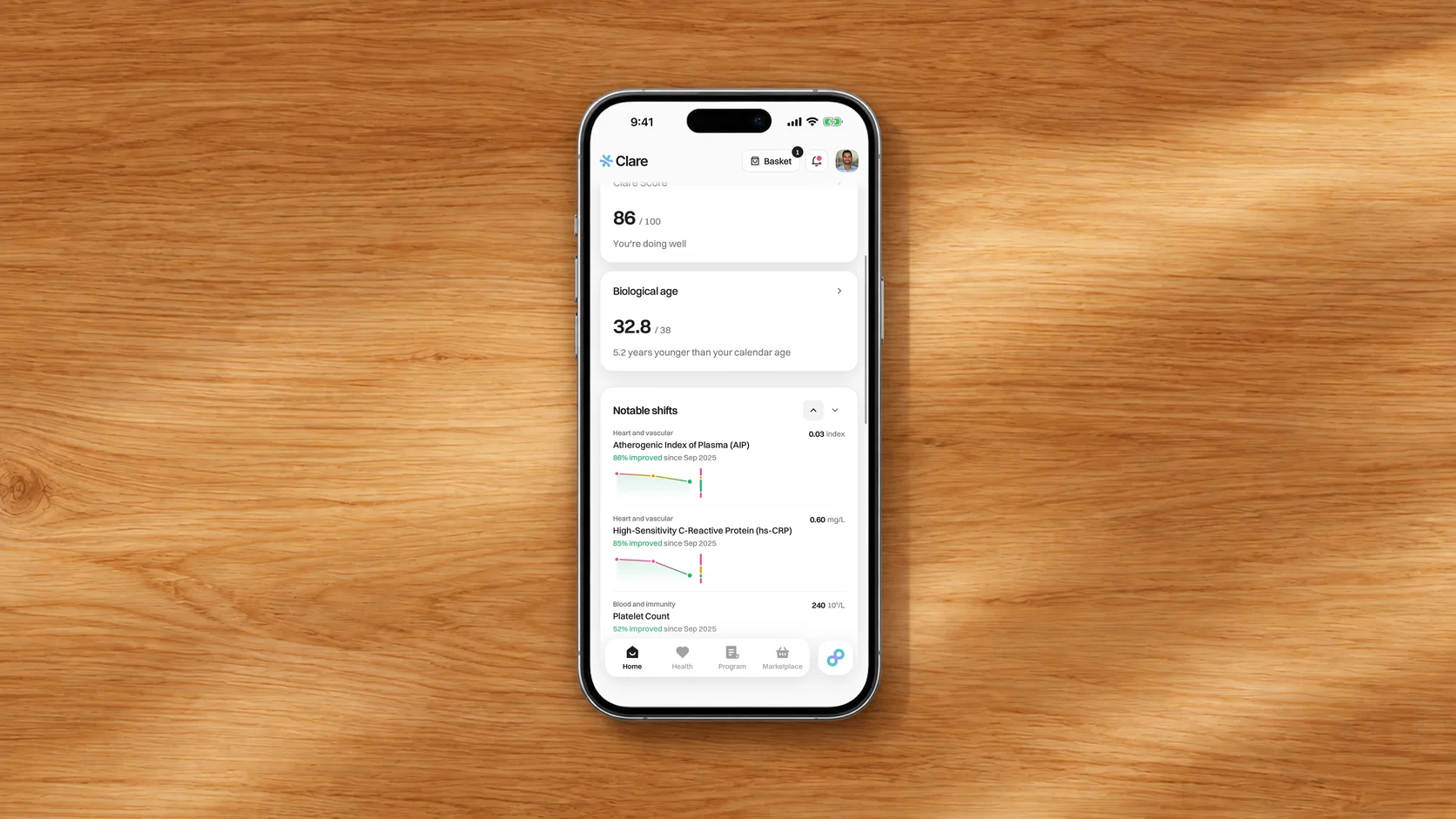 The Clare app on a phone lying on a wooden desk, its home screen showing a health score, biological age and recent blood test results.